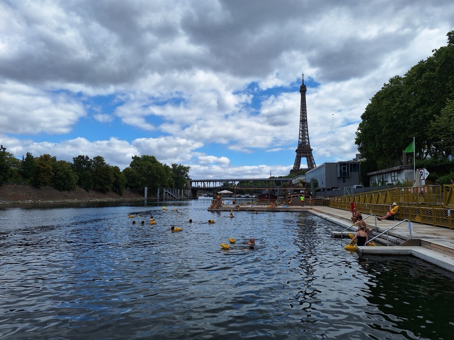Bathers with yellow tow floats in a pool created in the Seine, with the Eiffel Tower in the center of the frame
