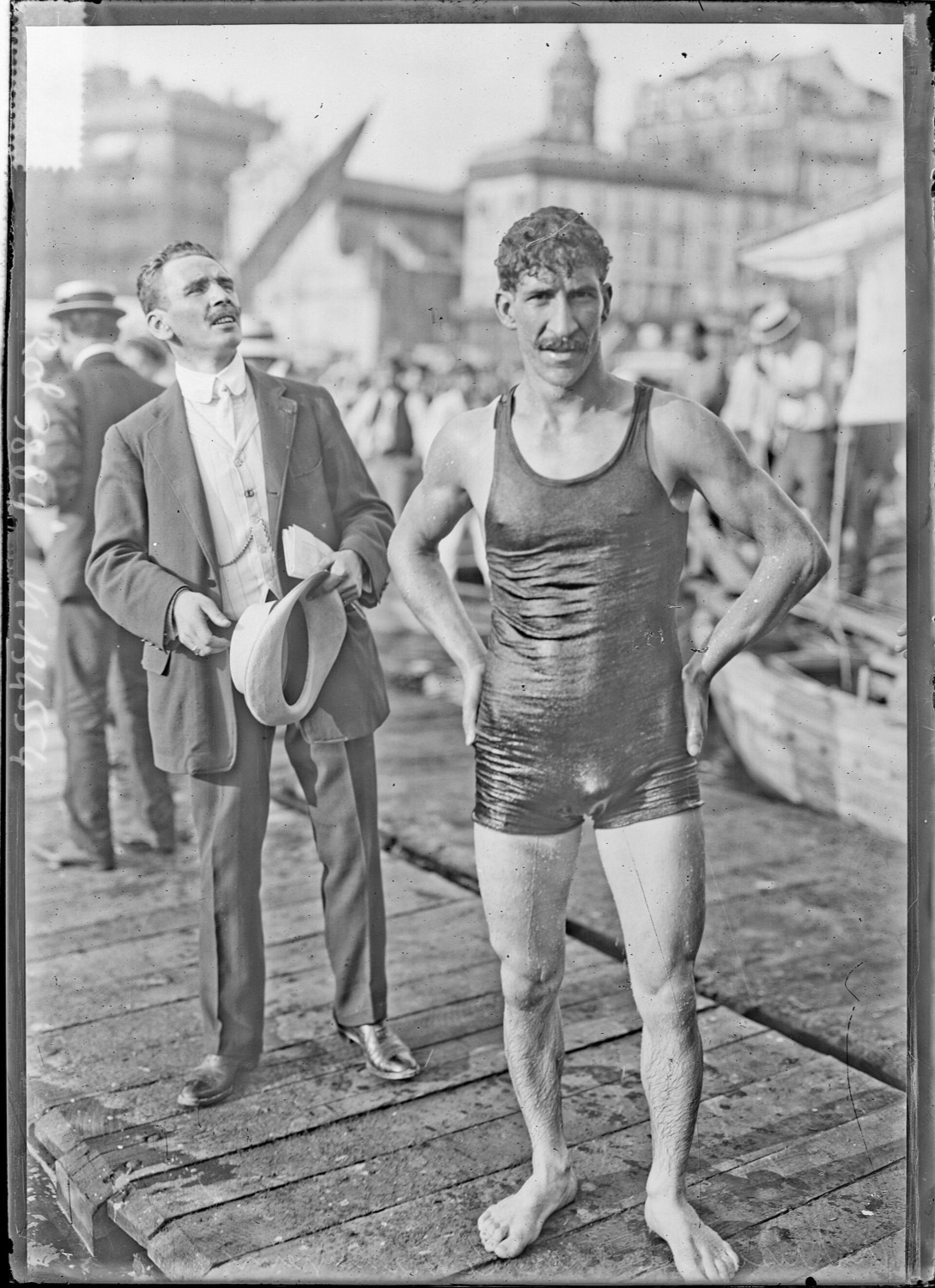Vintage photographic portrait of a swimmer in a dark full-body swimsuit, standing, arms at his sides
