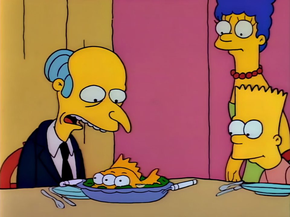 Still from The Simpsons: Mr. Burns sitting at the table in front of a plate with the cooked three-eyed orange fish, while Marge and Bart watch him standing behind his back